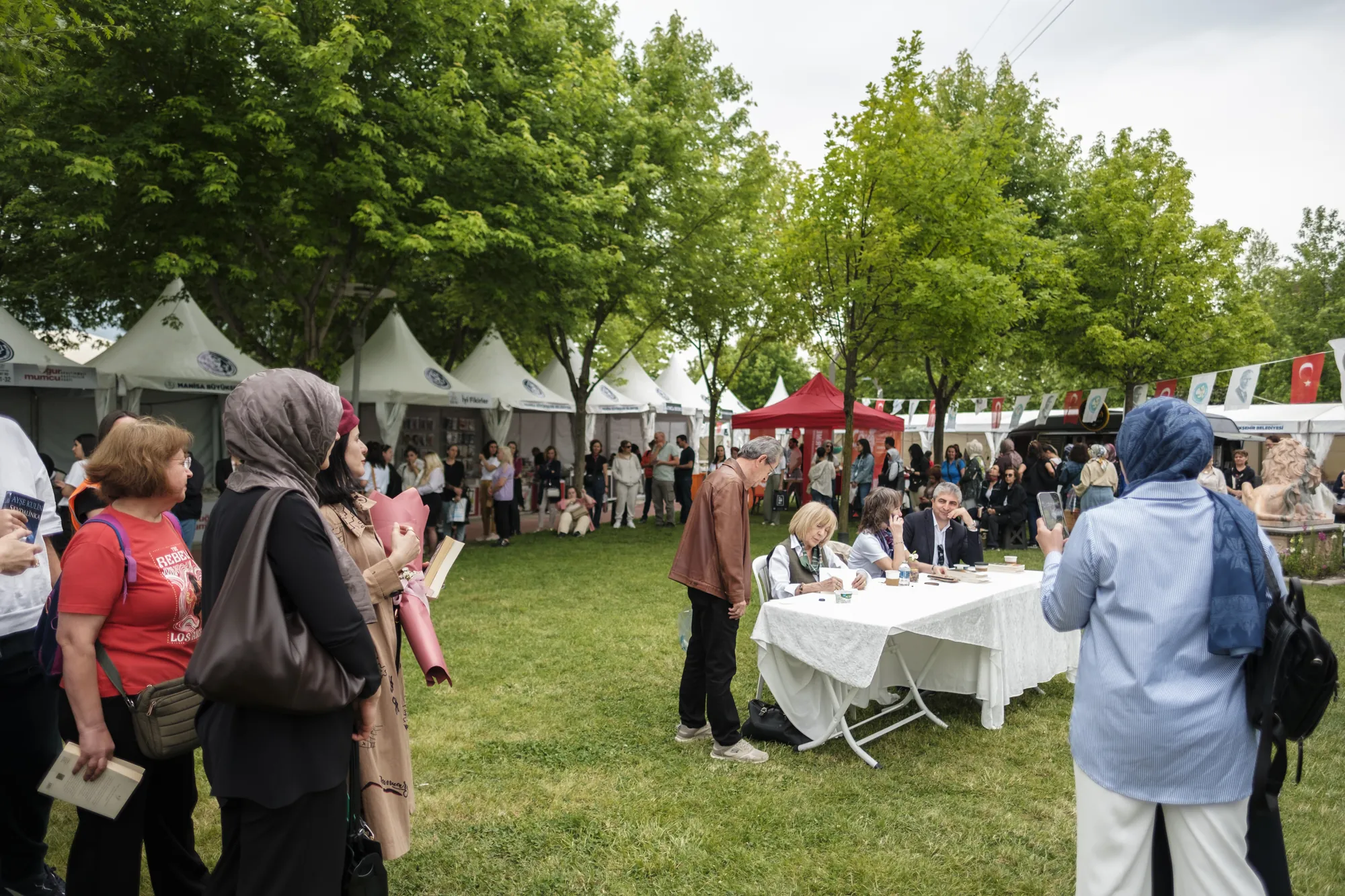 Çimenlik alanda kurulu imza masası ve etrafındaki ziyaretçiler