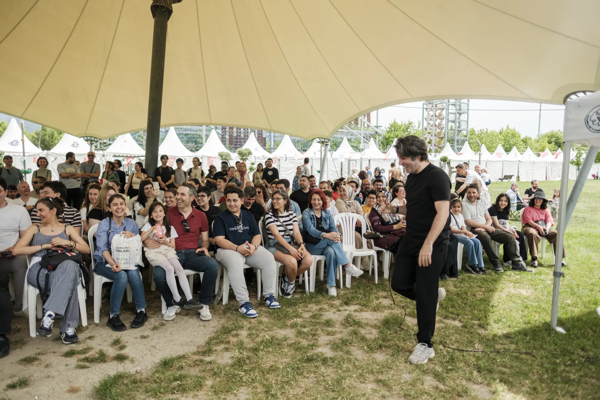 Çadır altında bir konuşmacıyı dinleyen izleyiciler